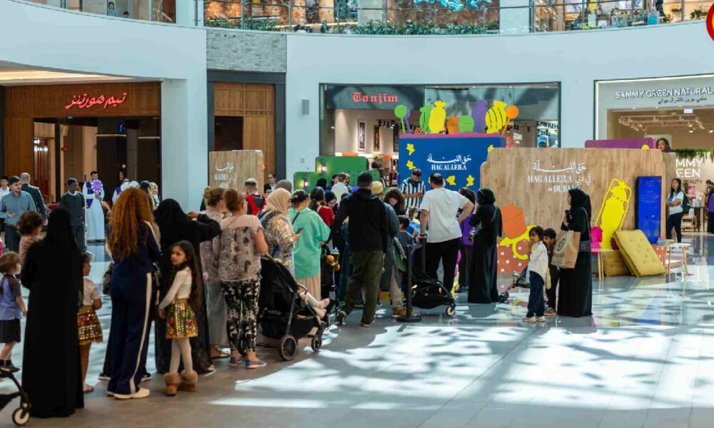 Families and children queue around a colourful HAG AL LEILA activation inside a Dubai shopping mall, where staff distribute sweets and lead festive activities in a decorated central atrium