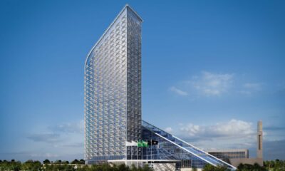 Exterior view of Sofitel Riyadh showing a tall, angular hotel tower with patterned facade, glass podium and Saudi flags at the entrance under a clear blue sky.