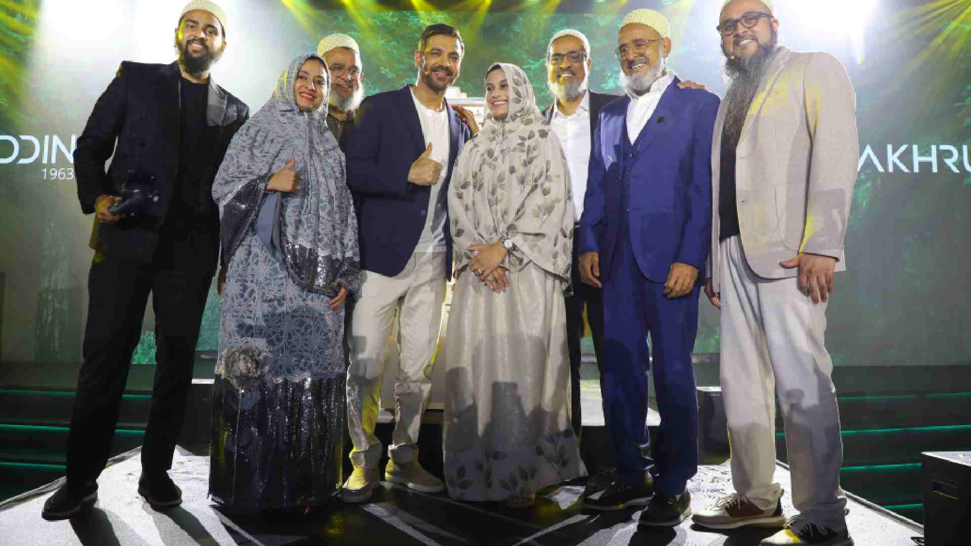 A group of formally dressed individuals standing together on a stage during a Fakhruddin Properties event, with bright spotlights and branded signage illuminated in the background.