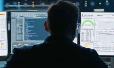 A person sits in front of multiple computer monitors displaying system dashboards, performance analytics, and code, monitoring data center operations inside a Vertiv facility.