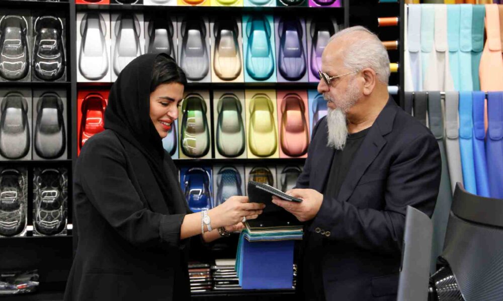 Two individuals reviewing material samples inside a design showroom, standing in front of a display wall filled with colorful leather swatches and automotive inspired panels.