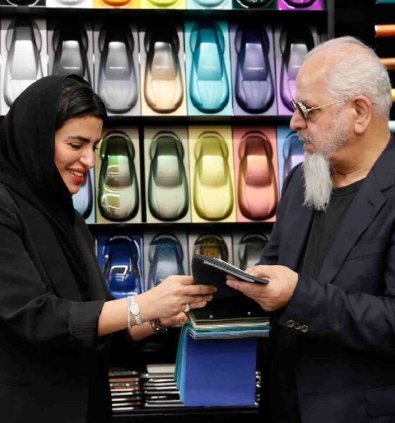 Two individuals reviewing material samples inside a design showroom, standing in front of a display wall filled with colorful leather swatches and automotive inspired panels.