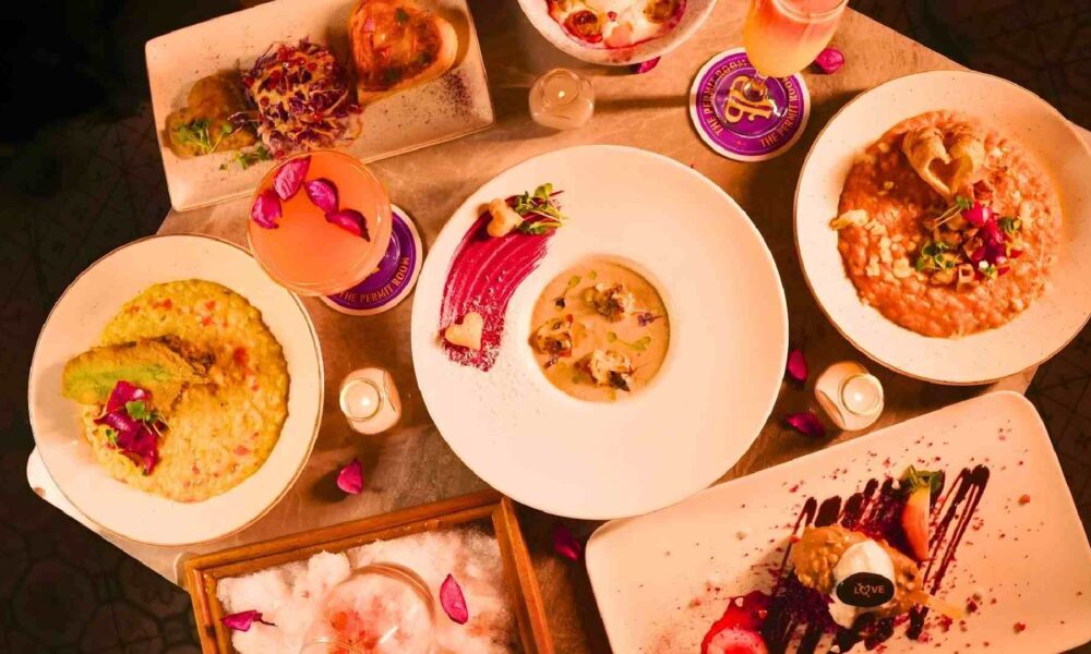 Overhead view of Valentine’s Week dishes and cocktails at THE PERMIT ROOM, featuring Indian mains, desserts with romantic plating, and pink-themed drinks on a dining table.