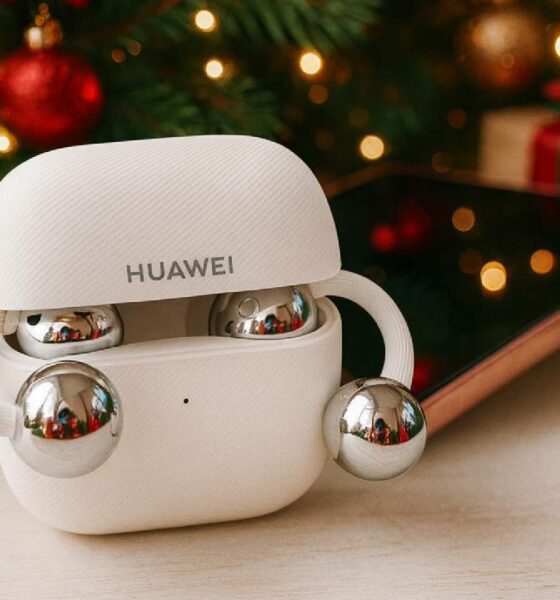 White HUAWEI FreeClip open‑ear earbuds inside an open charging case on a table, with a smartphone, Christmas tree, lights, and wrapped gift boxes in the background.