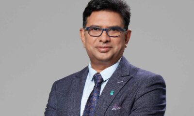 Ravi Tallamraju, Chief Technology Officer at Petronas Lubricants International, standing with arms crossed in a navy suit against a neutral studio background, wearing a Petronas lapel pin and wristwatch.